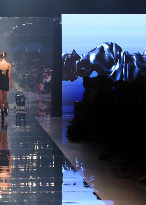 Black dress High heels Model walk back on mirror Runway Fashion Show catwalk with reflection on floor lighting along walk way, background stage ramp, copy space for text logo